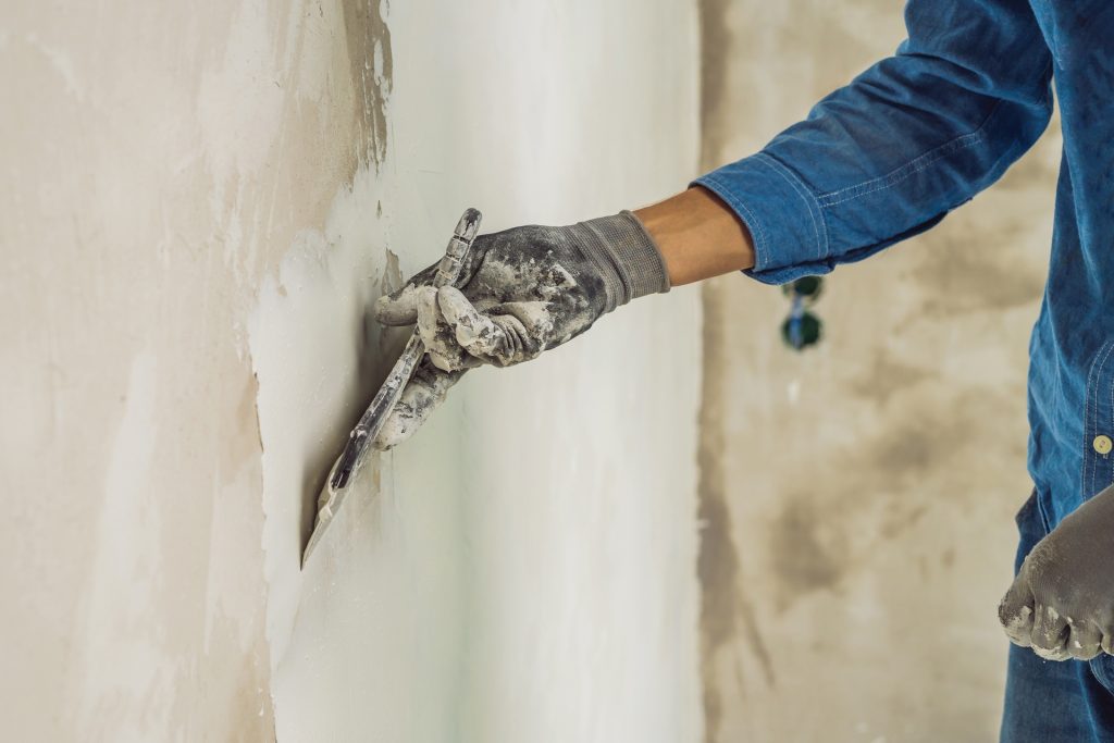 master is applying white putty on a wall and smearing by putty knife in a room of renovating house in daytime